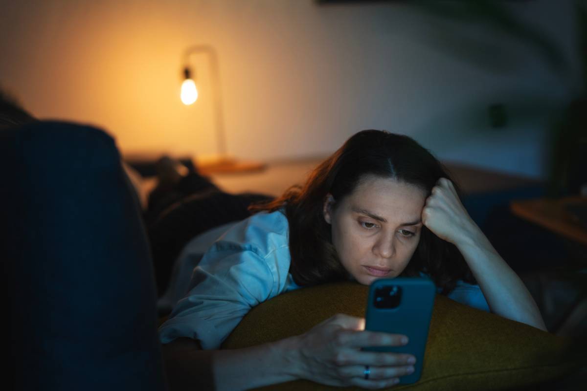 暗い部屋で布団に入りながらスマートフォンを見る女性