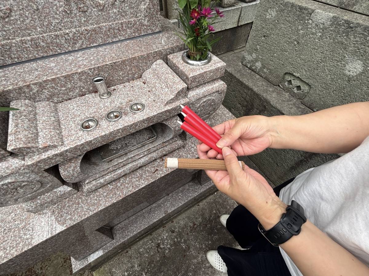 お墓前でお線香とろうそくを持っている写真