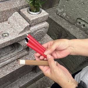  お墓前でお線香とろうそくを持っている写真 