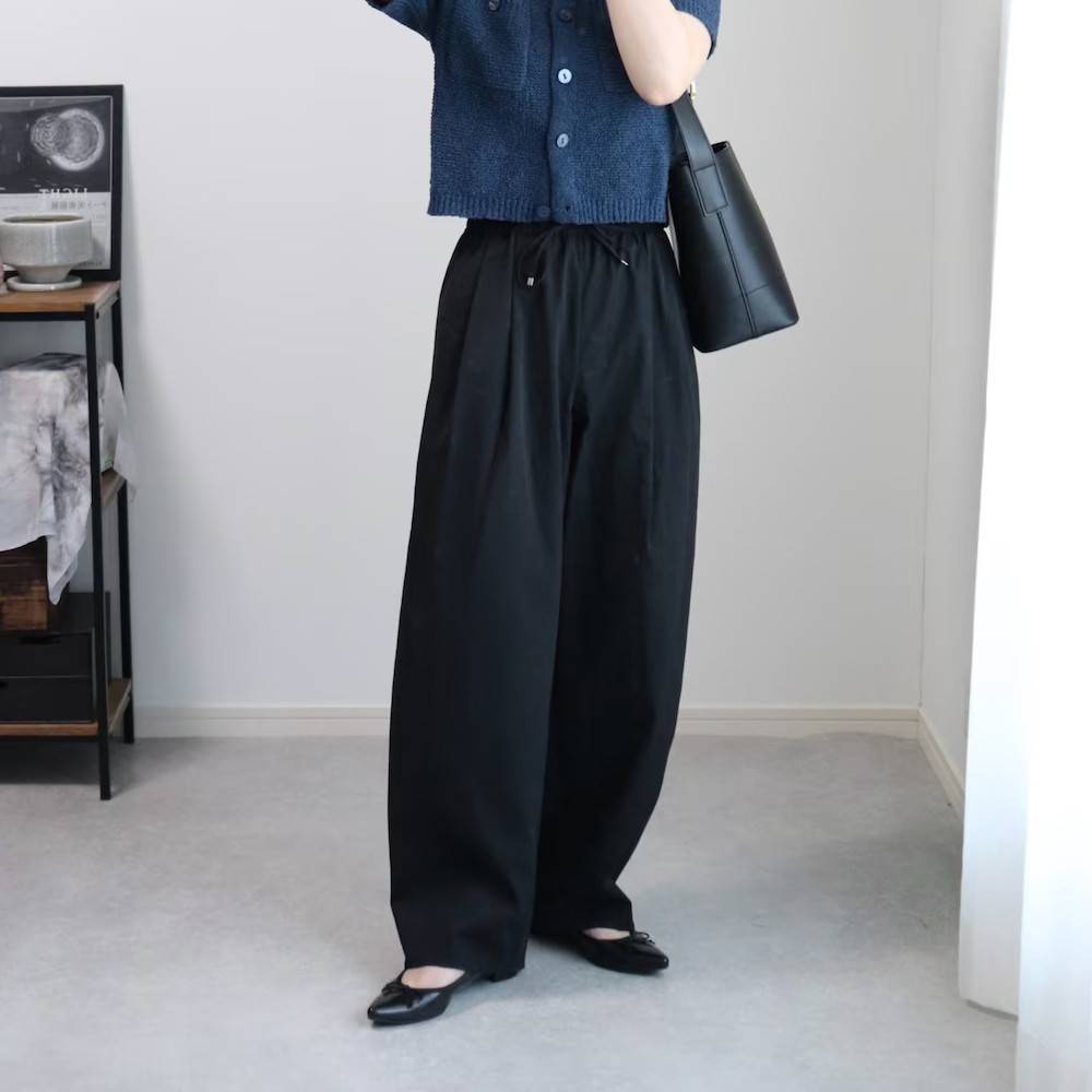 ブルーのカーディガンに黒パンツを合わせた女性