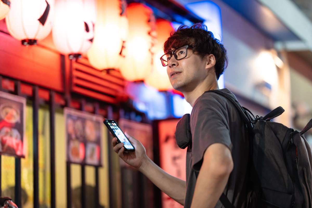 居酒屋の前でスマートフォンを持っている男性