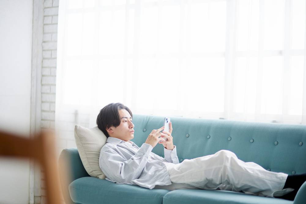 ソファで横たわってスマホをする男性