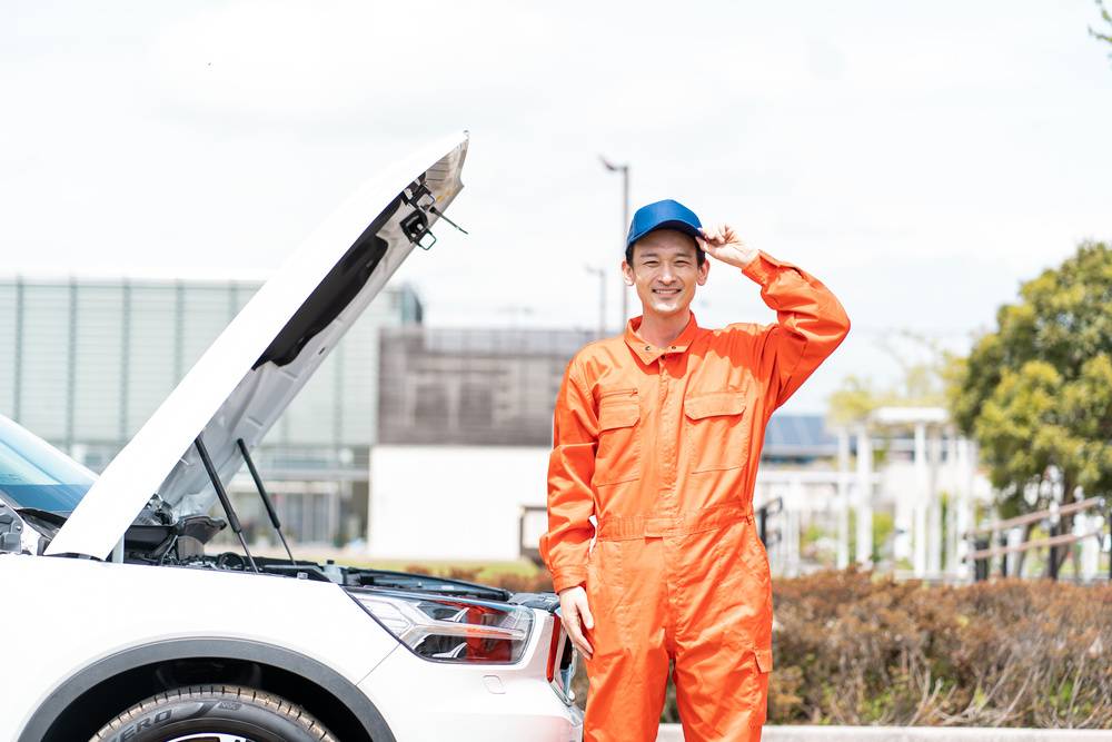 車の前に立つ作業着を着た男