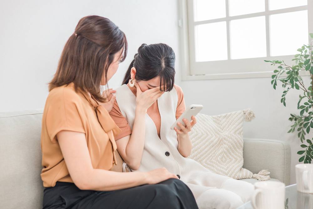 スマホを見て落ち込む女性と慰める女性