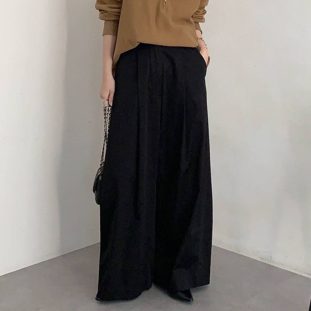 キャメルのトップスに黒パンツを合わせた女性