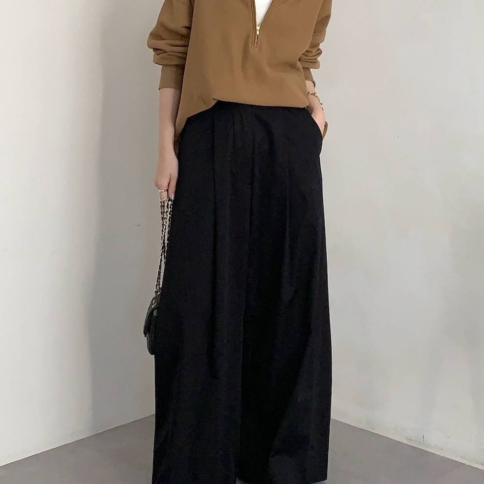 キャメルのトップスに黒パンツを合わせた女性