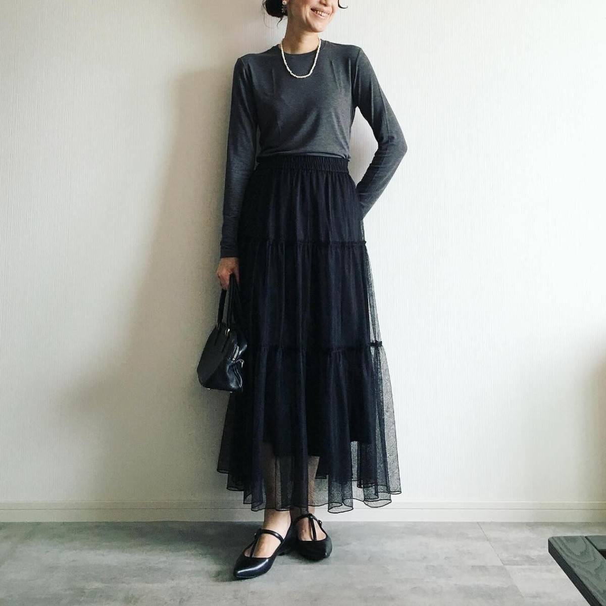 グレーのトップスに黒スカートを合わせた女性