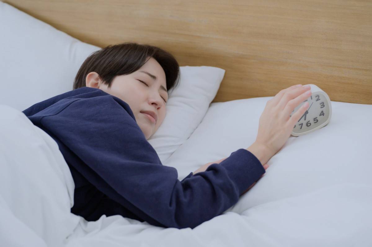 眠そうに目覚まし時計を止める女性