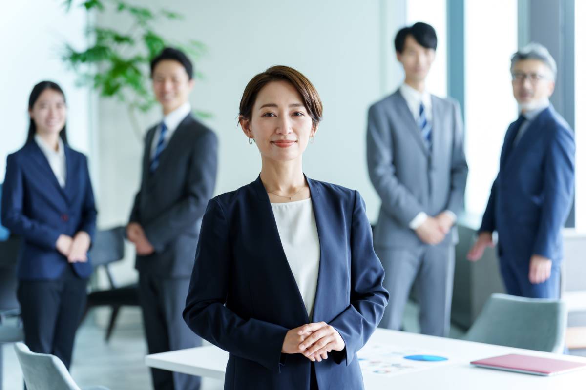 社員に囲まれたスーツ姿の女性